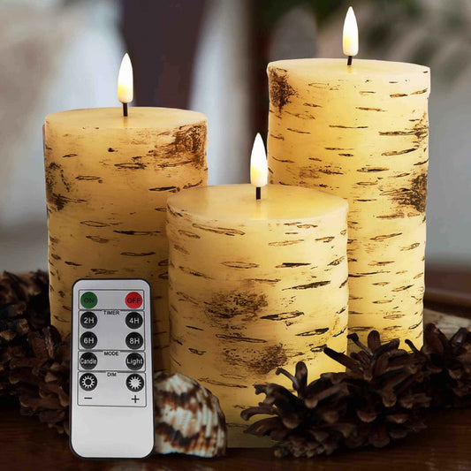 A set of three birch pattern flameless pillar candles in different lengths and a remote control, along with some brown plants and seashells, on a table