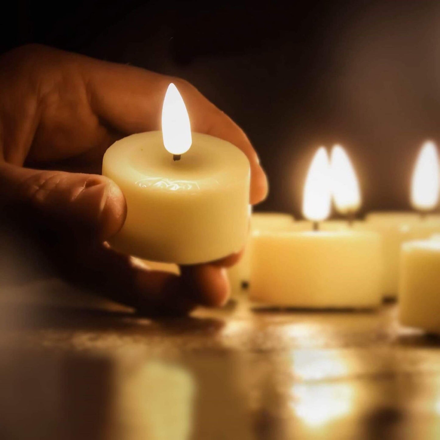 There are some lit eywamage led tealights on the table and a hand picks up one of the candles