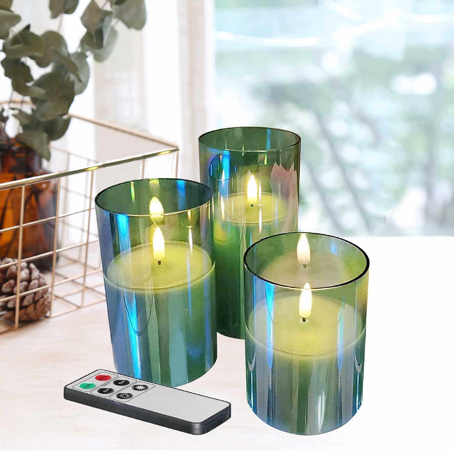 3 eywamage green glass flameless candles and a remote control on a table, behind a basket with greenery and pine cones