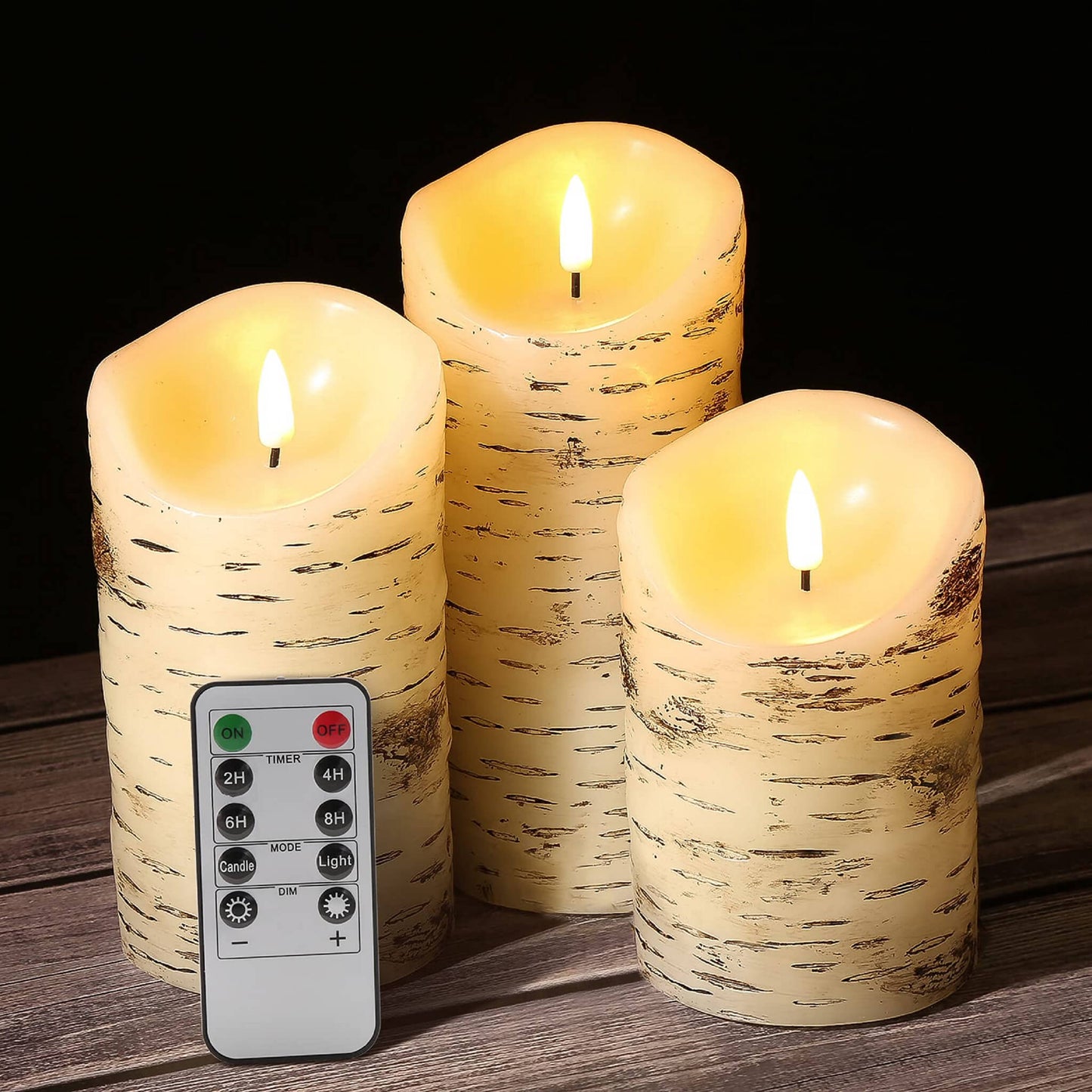 Three melted top birch pattern pillar candles and a remote control on a wooden table