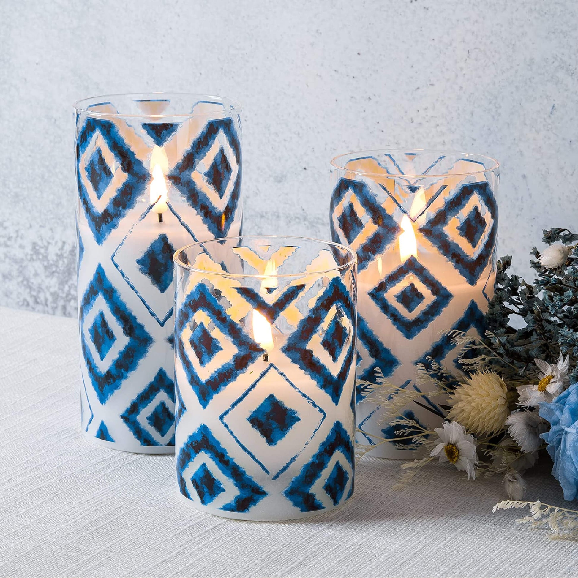 3 lit Flickering Blue White Geometric led candles on a white tablecloth next to a bouquet of flowers