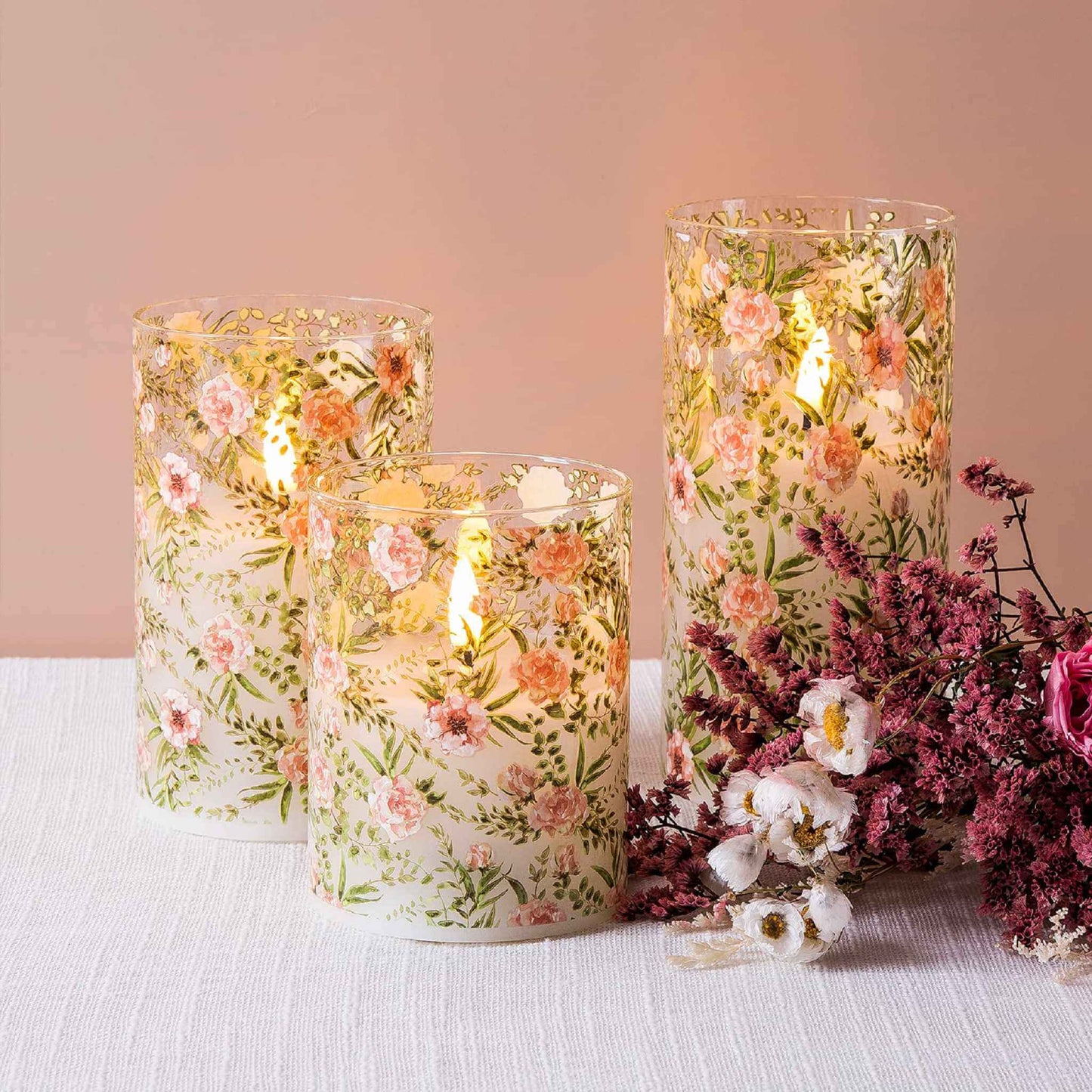 Three eywamage floral glass flameless candles lie on a white tablecloth with a bouquet of white and pink flowers next to them