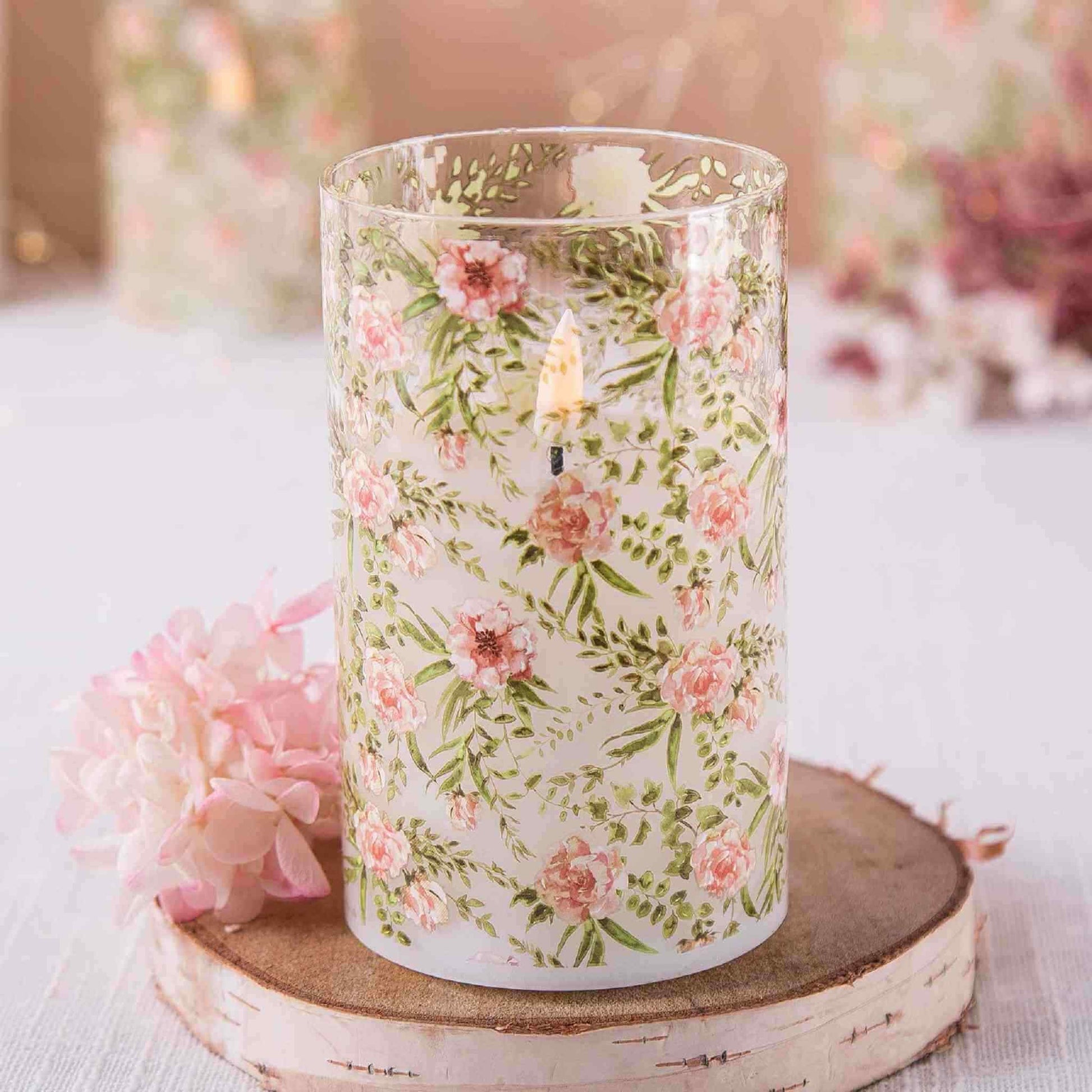 An eywamage floral glass flameless candle and a pink flower rest on a circular wooden board.