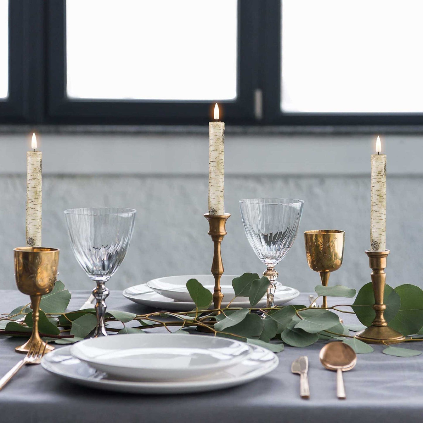 A beautifully set dinner table with elegant white plates, silverware, and wine glasses, surrounded by LED taper candles.