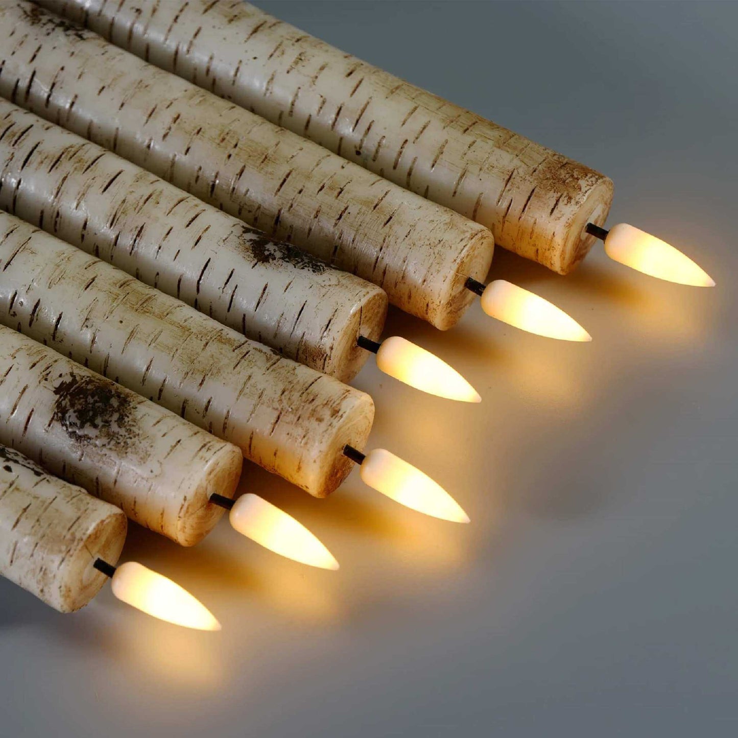 Flameless tapered candles in a birch pattern, lit and placed side by side on a table
