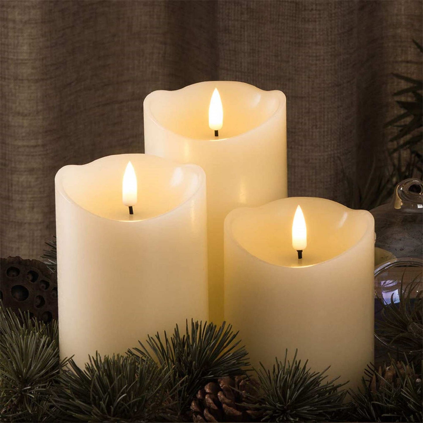 3 led ivory timer flameless pillar candles, surrounded by pine branches and glassware for decoration