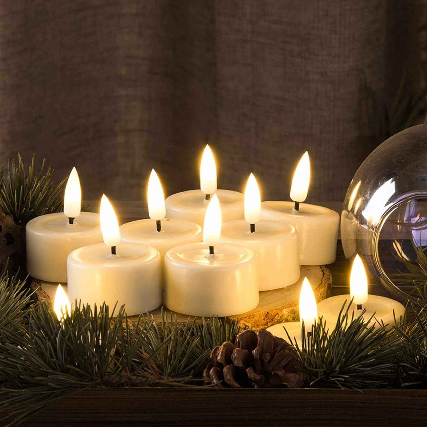 10 led tealights are lit and placed on a tree stump surrounded by pine branches and a glass vessel