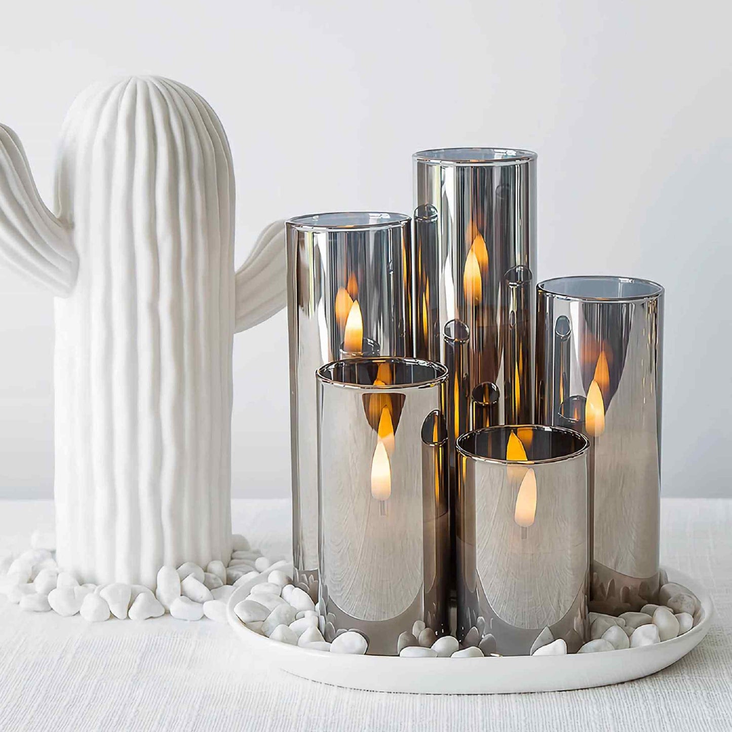 A set of three slim grey LED pillar candles, displayed on a wooden tray with decorative cactus accents