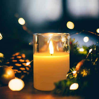 The table has a lit clear glass flameless candle at night surrounded by some night lights and pine branches