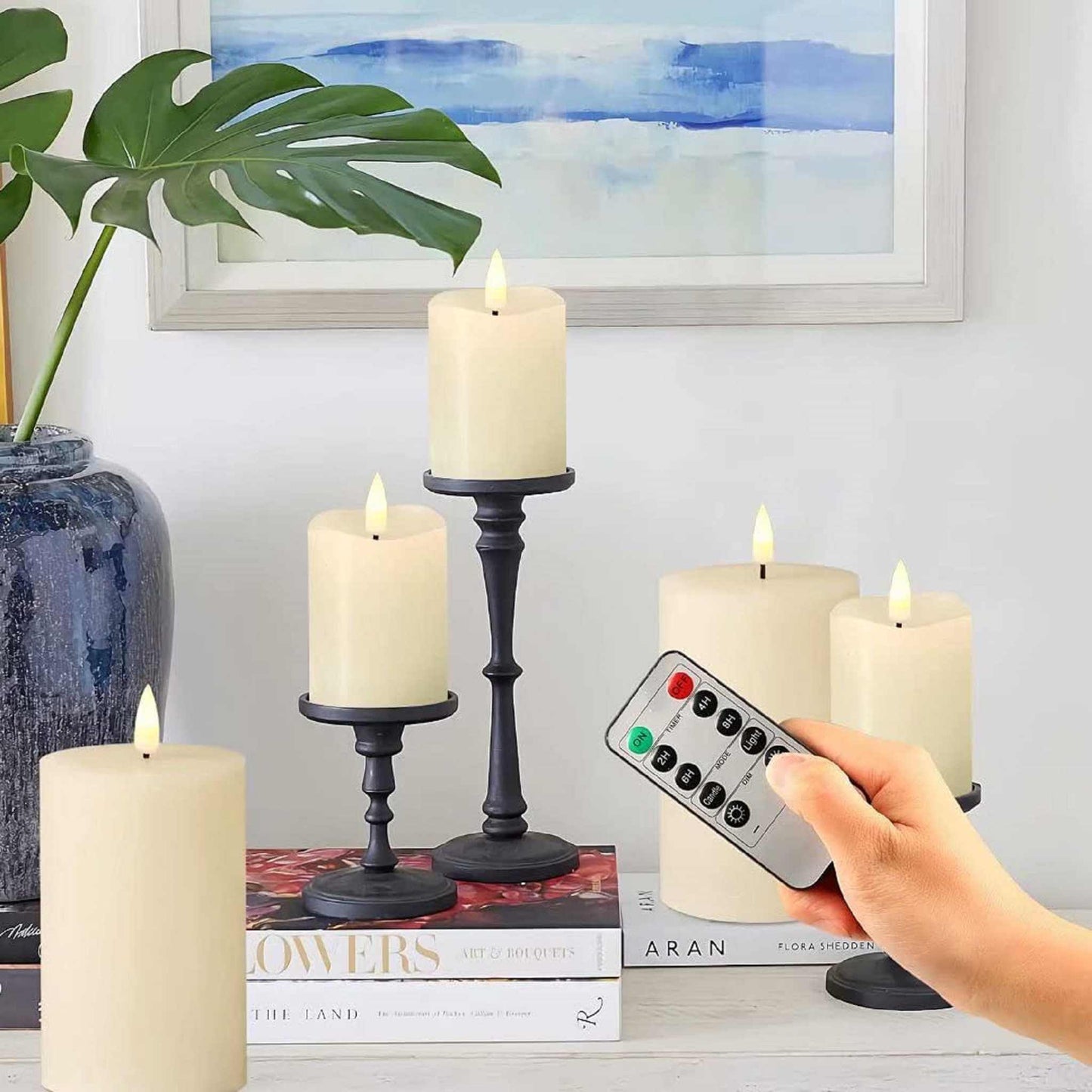 eywamage Flameless Votive Pillar Candles on top of books on a table next to a vase with decorative paintings of clothes on the wall