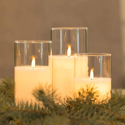 Three lit clear glass flameless candles on a pile of pine branches