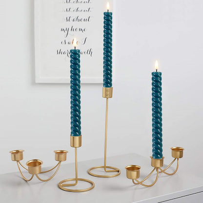 There are four candlesticks on a pure white table with three lit eywamage blue spiral flameless taper candles