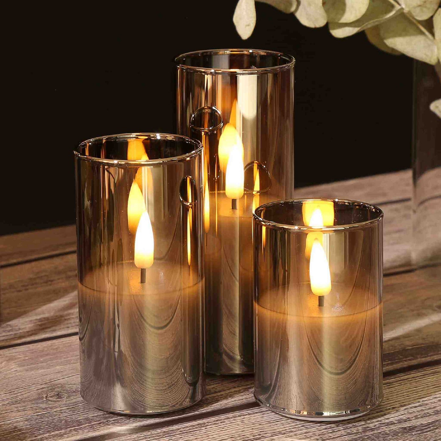 Three gray glass electric candles on a table with some greenery